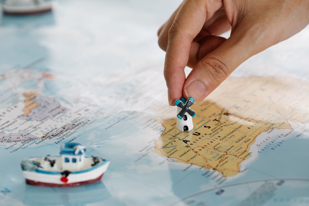 Close-up of a hand placing a tiny windmill on a map, highlighting Australia.
